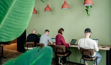 Vier Personen, die nebeneinander an einem Arbeitstisch vor ihren Laptops sitzen.