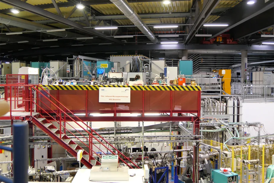 Experimentierhalle mit Maschinen, Rohren und einer roten Metalltreppe zu einer erhöhten Plattform