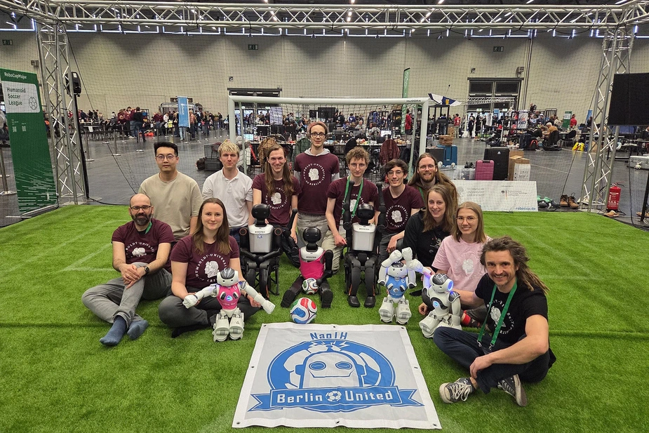 Das 12-köpfige Team mit den Fußballrobotern auf dem Kunstrasen in einer Halle