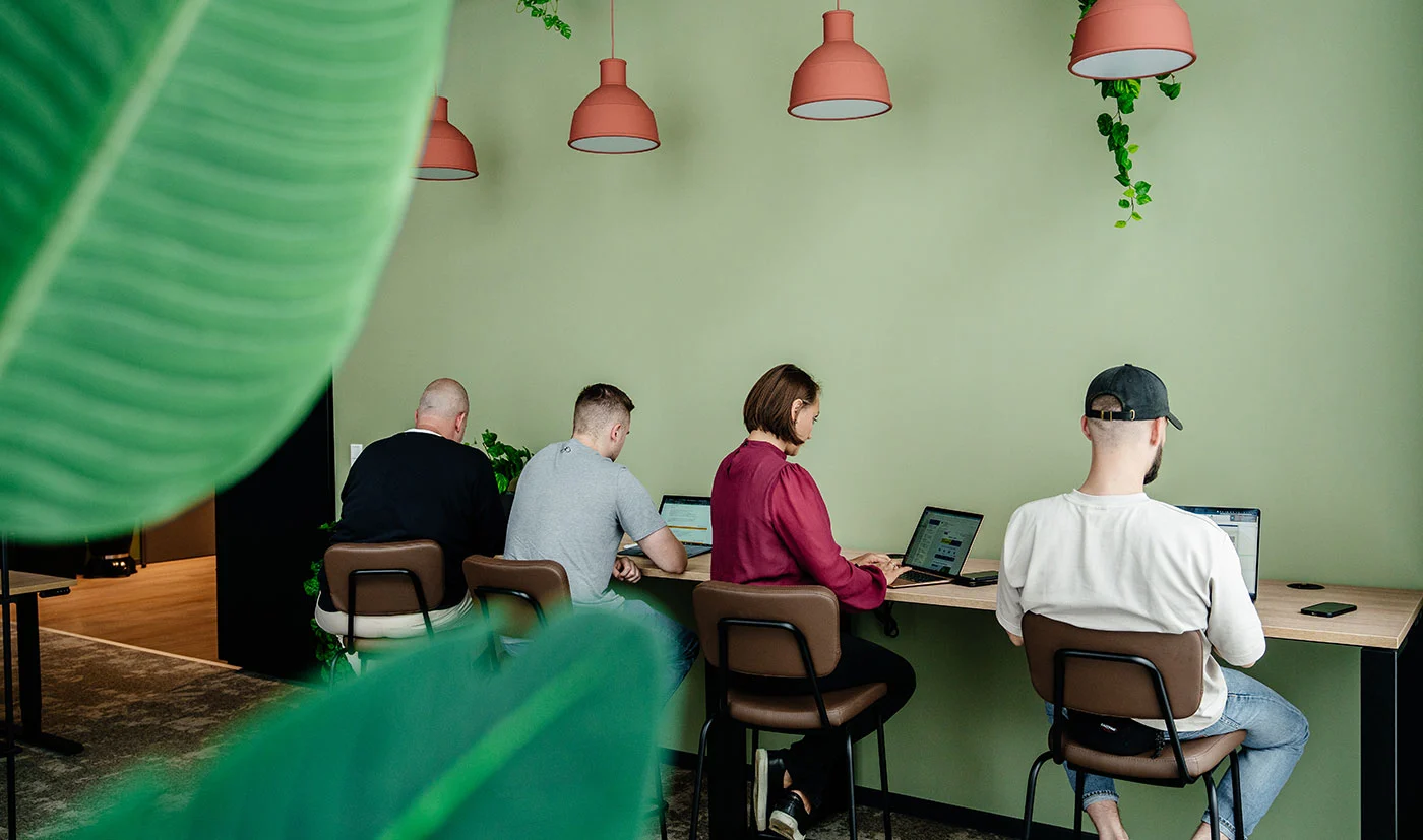 Auf dem Bild sind vier Personen von hinten zusehen, die an einem hohen Arbeitstisch im CHIC Coworking Space sitzen und arbeiten.
