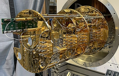 Goldfarbener Kryostat mit zahlreichen Drähten und Kabeln, montiert in einem großen, runden Gehäuse