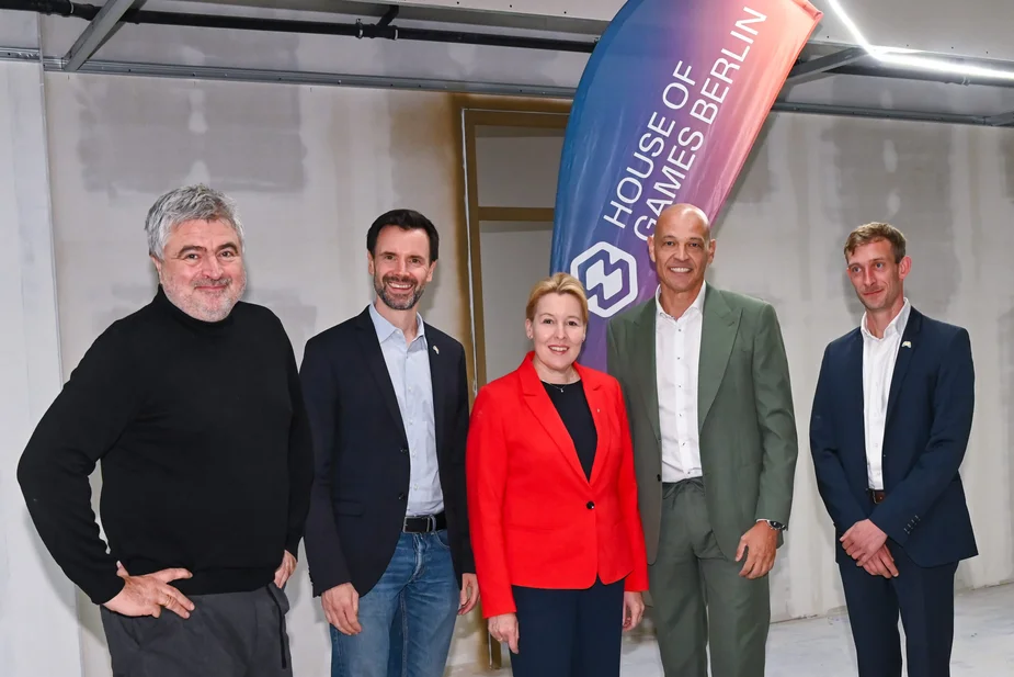 Gruppenfoto vor einer unverkleideten Wand und einem Banner des House of Games Berlin