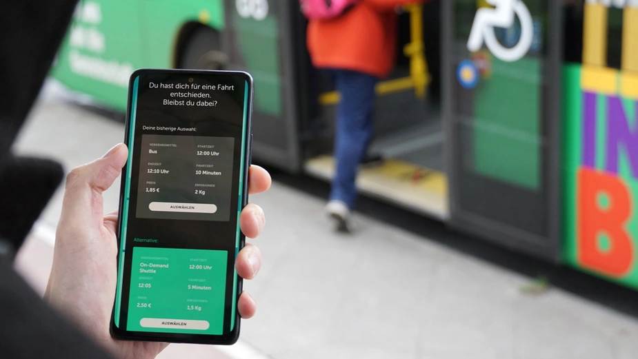 A smartphone in someone’s hand; in the background, a person is getting on a bus