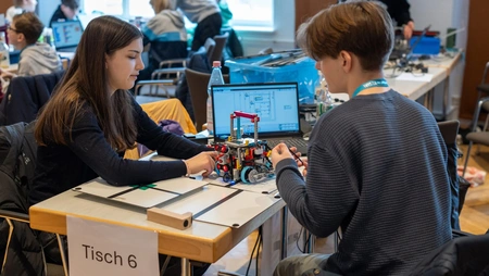 Schüler:innen sitzen am Tisch und bauen an ihren Robotern