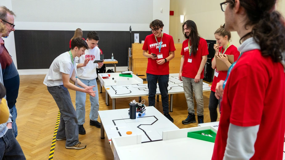 Zwei Schüler fiebern an einem Tisch, auf dem der Roboter fährt, unter den Augen der Jury