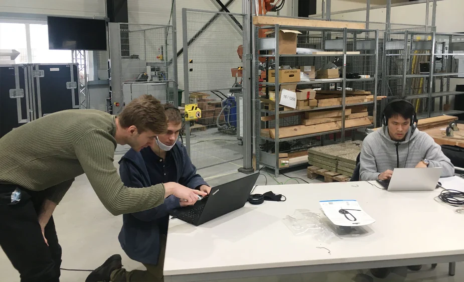 In einer Halle sitzen an einem Tisch drei Mitarbeitende der PTXtech GmbH an Laptops und arbeiten.